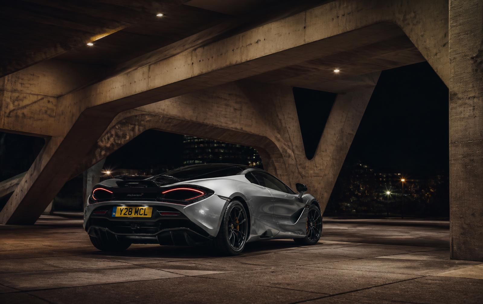 Silver supercar parked under brutalist concrete architecture at night