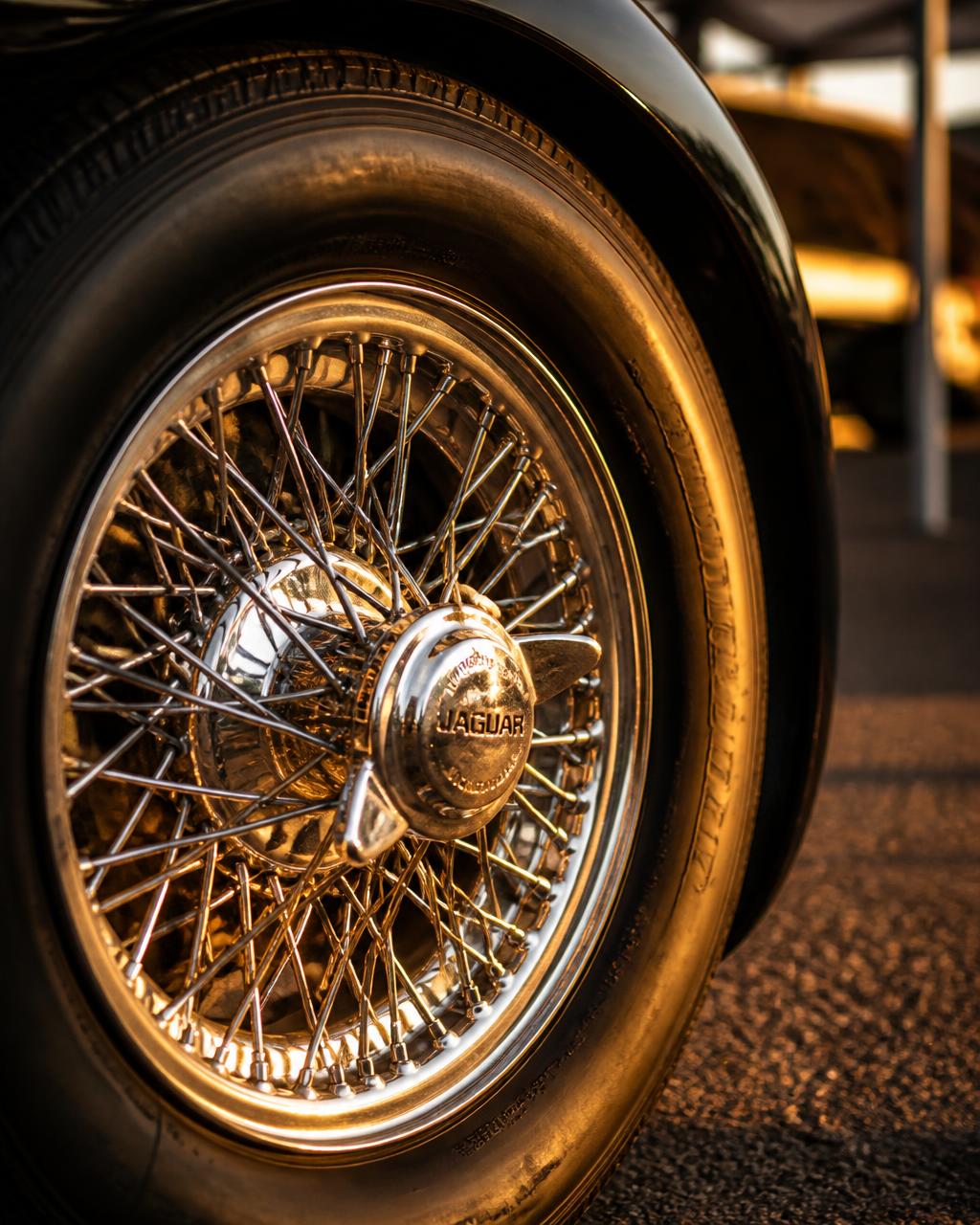 Close crop of a chrome wire wheel on a classic car with warm golden reflections